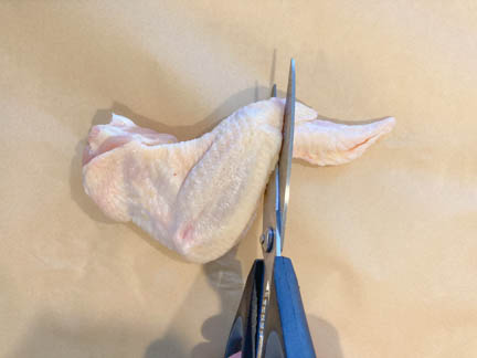 raw chicken wing with kitchen shears showing where to clip