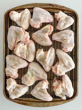 raw chicken wings on rack sprinkled with seasonings