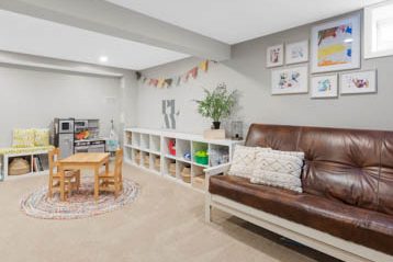 Playroom with kids table and toys with brown leather couch and kids artwork in frames displayed on wall above couch