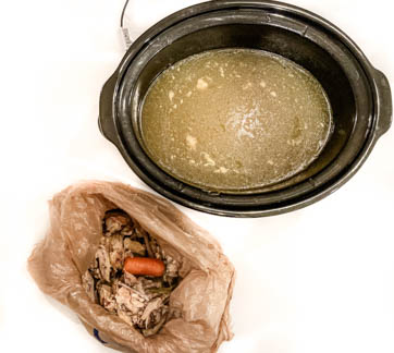 birds eye view of slow cooker with bone broth and plastic bag with food scraps on white counter