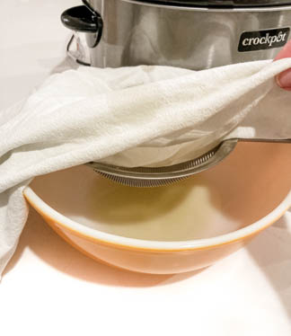 orange bowl on top of white counter showing wire strainer lined with white cloth