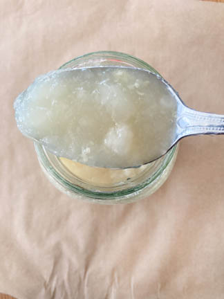 Silver spoon holding chicken bone broth over glass jar on brown counter