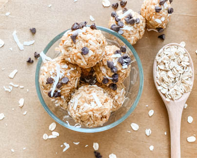 no bake peanut butter treats in glass bowl with wooden spoon full of rolled oats next to it