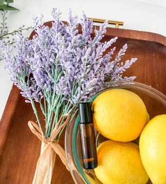brown tray holding bunch of lavender and clear bowl of lemons with brown roller bottle on top