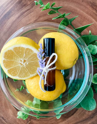 clear bowl holding lemons with brown essential oil roller bottle on top 