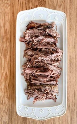 White platter with cooked shredded beef brisket on wood table 