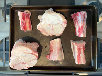 raw beef marrow bones on baking sheet on top of gas oven