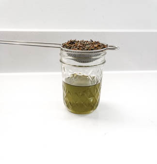 fine mesh strainer straining herbs into small glass jar