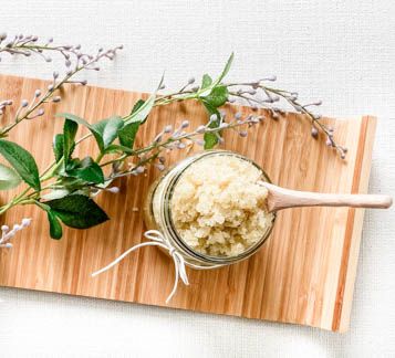 lavender sprig next to glass jar with brown sugar scrub and wooden spoon