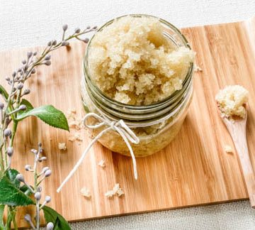 natural sugar scrub in glass jar next to lavender sprig and wooden spoon