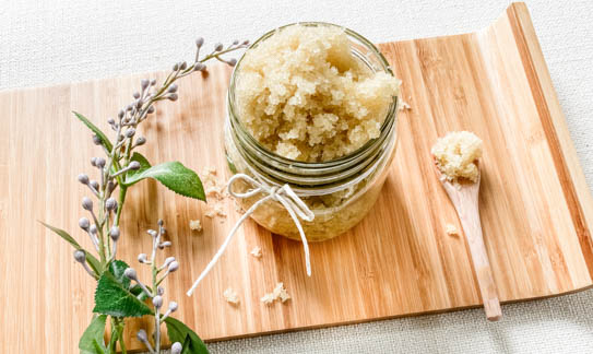 natural sugar scrub in glass jar next to lavender sprig and wooden spoon
