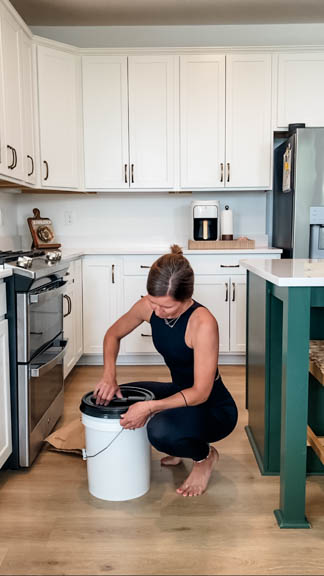 woman screwing black lid onto white 5 gallon bucket in kitchen