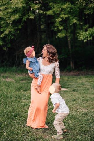 woman standing on grass  in orange and white dress with toddlers in front of green tress
