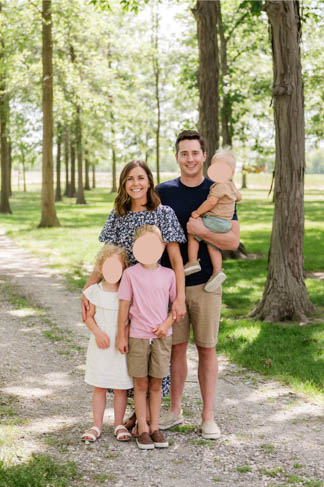 young family picture in the woods featuring mom with arms around two kids and dad holding baby.