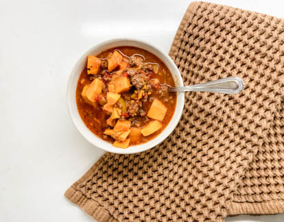 white bowl full of sweet potato chili next to brown kitchen towel
