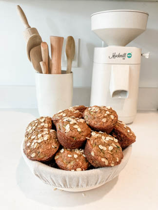 fresh milled einkorn zucchini muffins in a bowl in front of utensil holder and grain mill