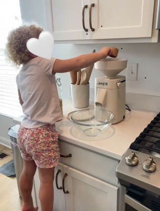 Shows back of young girl in flour shorts and t-shirt milling flour with home mill