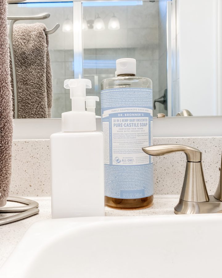 white soap dispenser on bathroom counter next to hanging hand towel and faucet